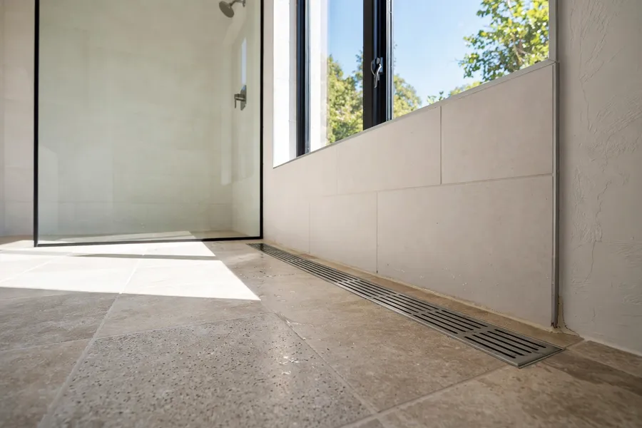 Linear drain along the wall of a curbless shower floor