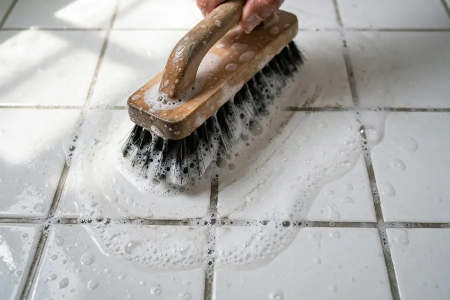 Stiff brush scrubbing floor grout lines with soapy water