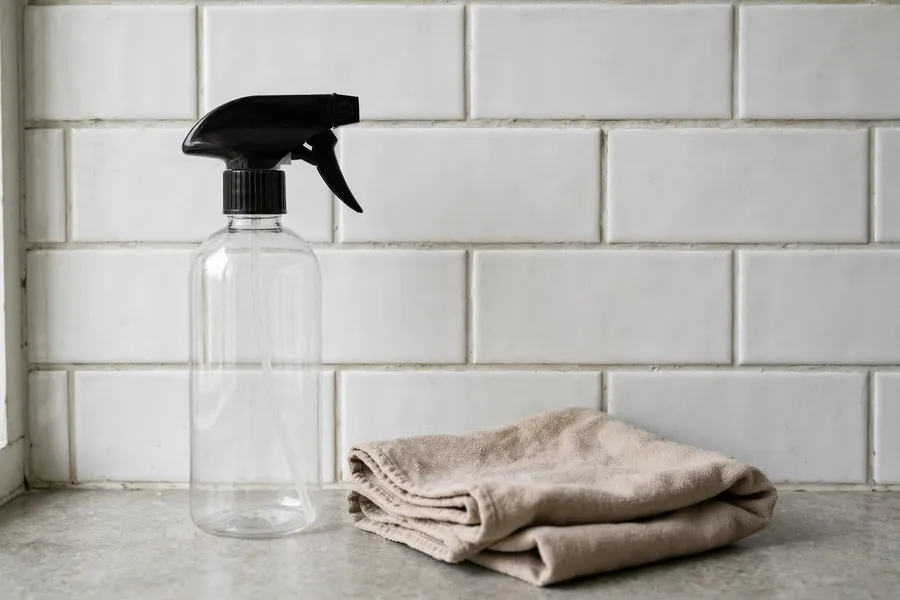 Unmarked spray bottle and cloth beside a bathroom tile wall