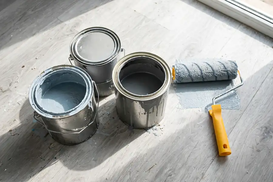 Floor paint cans and a roller next to a vinyl floor
