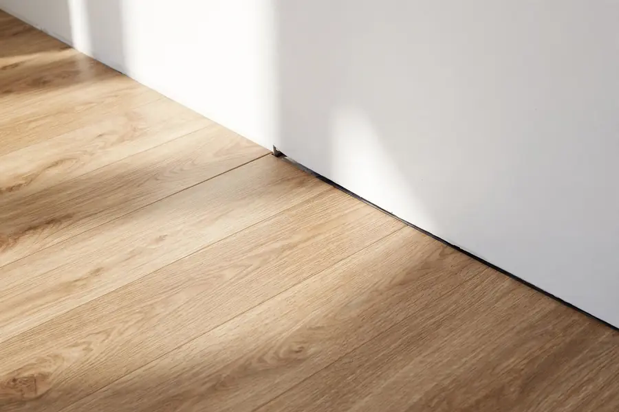 Laminate flooring laid along a wall with a small expansion gap at the edge