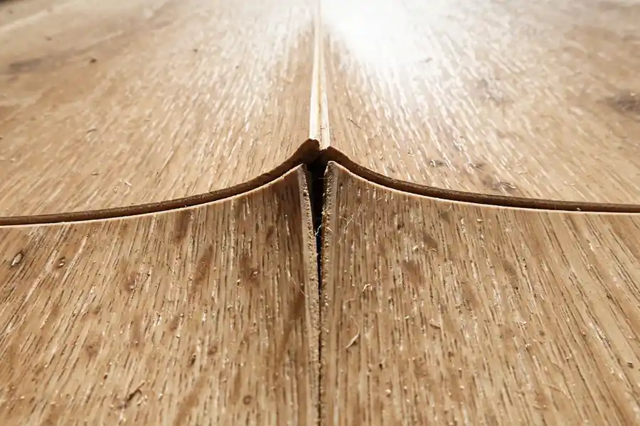 Close-up of laminate flooring with a raised ridge peaking at a seam