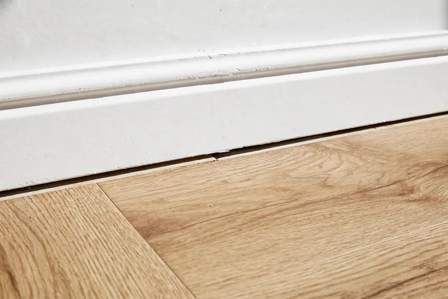 Vinyl plank flooring meeting a wall with a baseboard and a small expansion gap