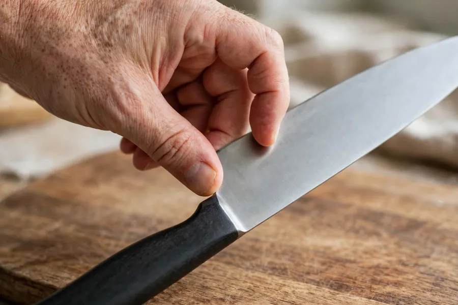 Hand holding a chef knife in a pinch grip above a wooden cutting board