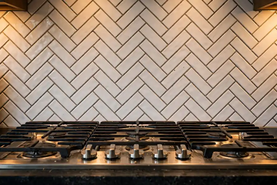 White subway tile backsplash in a herringbone pattern with grout lines behind a gas stove