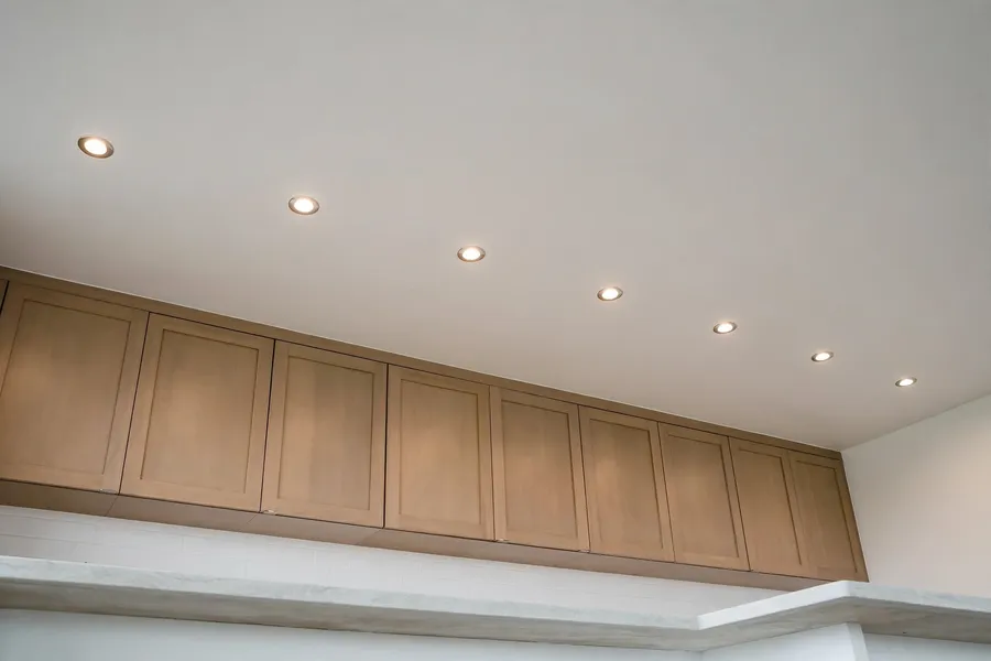 Recessed downlights spaced evenly in a row across a kitchen ceiling above wall cabinets