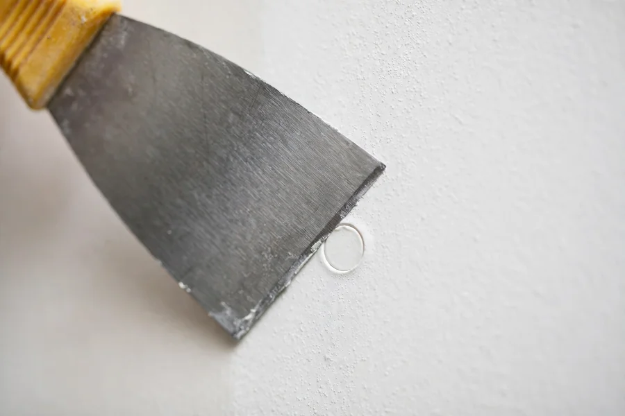 Putty knife filling a nail hole flush with the wall